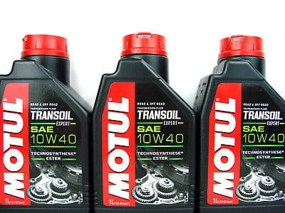 Three black plastic bottles of MOTUL 105895 Transmission Oil, 10W-40, with red caps, featuring a label with bold white and red text, and a gear graphic, each with a 1-liter capacity.