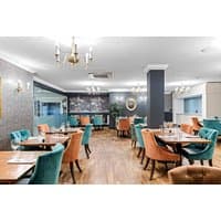 Elegant dining area at The Dukes Head Hotel with teal and orange chairs, wooden tables, and chandeliers.