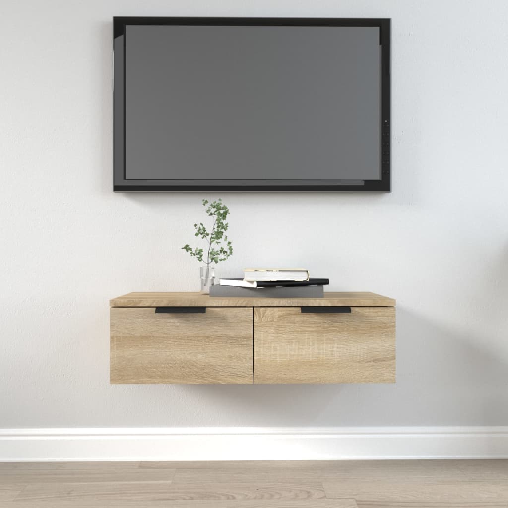 Sonoma oak wall cabinet in brown engineered wood, featuring two drawers with black handles, mounted below a flat-screen TV, with decor items on top.