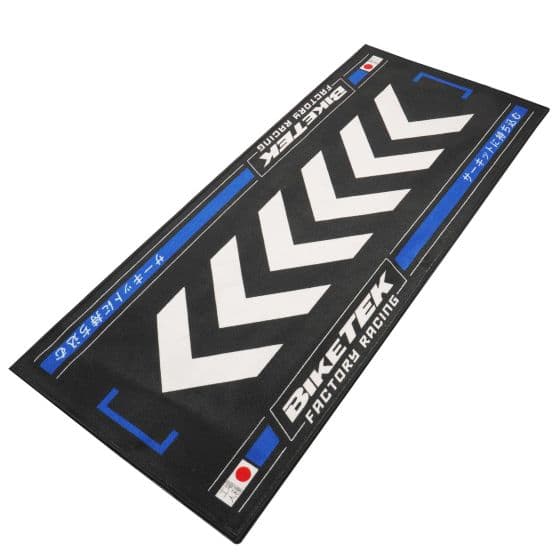 Black carpet featuring bold white chevron patterns and blue accents, labeled "BIKETEK FACTORY RACING," designed for environmental use in a biking context.