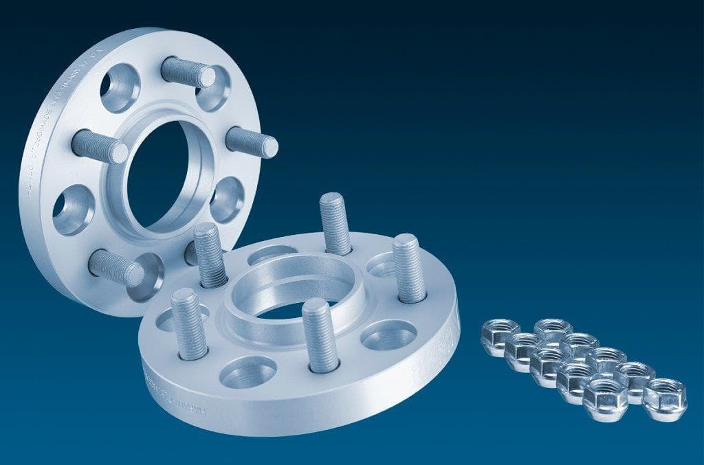 Silver aluminum wheel spacers with five bolt holes, 20mm thickness each, designed for track widening, accompanied by matching nuts, set against a dark blue background.