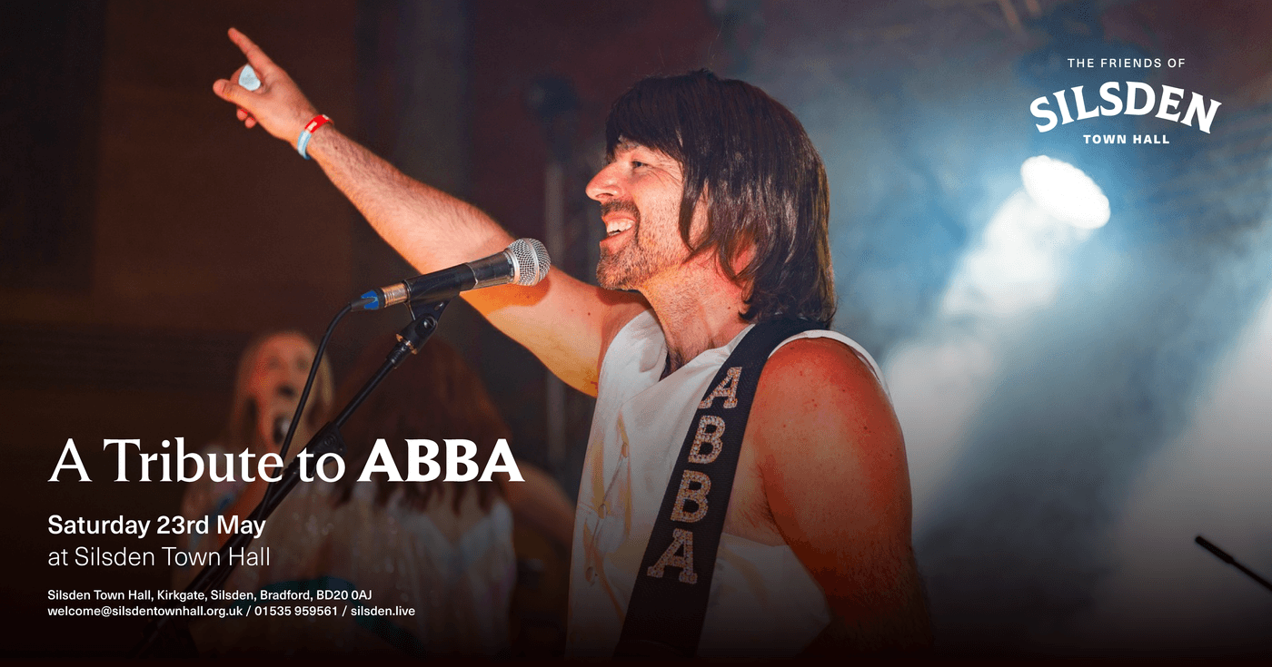 A lively performance at Silsden Town Hall, with a singer in a wig and ABBA-themed attire, capturing the festive atmosphere.