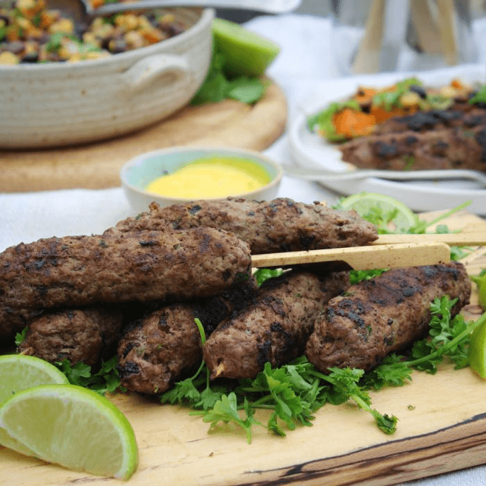 Grilled kebabs on a wooden board, garnished with fresh herbs and lime wedges, set against a vibrant summer picnic backdrop.