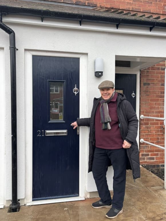 A man stands at the entrance of a refurbished apartment in Yorkshire, showcasing modern architecture and welcoming atmosphere.