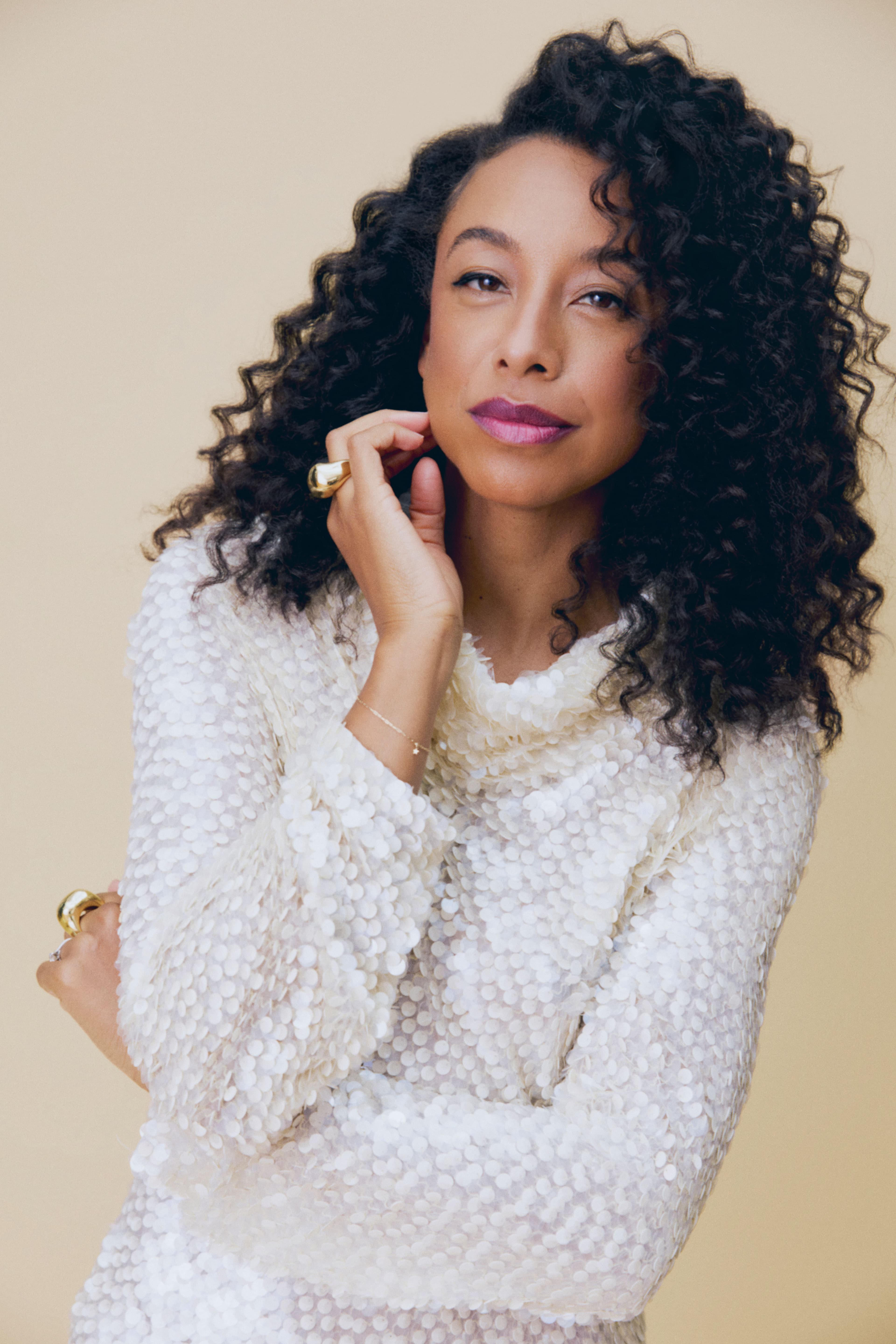 Corinne Bailey Rae poses confidently in a shimmering white top against a soft beige background, exuding elegance and charm.