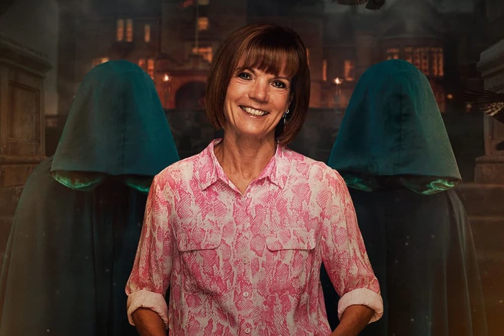 A smiling woman in a pink shirt stands in front of two cloaked figures, set against a dark, atmospheric backdrop.