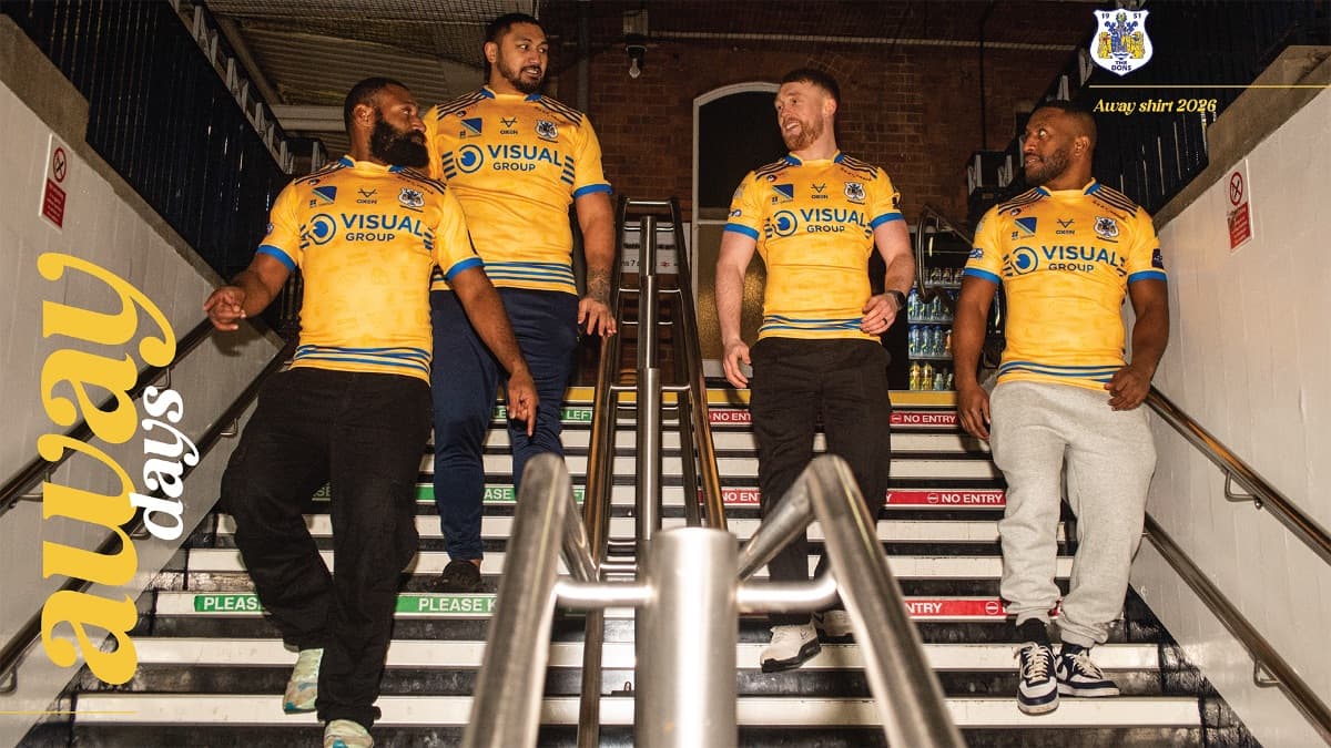 Four fans in vibrant yellow away shirts descend a stairway, showcasing team spirit and camaraderie in a lively atmosphere.