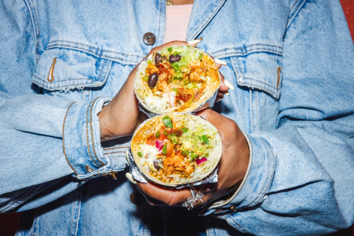 Two delicious burritos filled with rice, beans, chicken, and guacamole, held by hands in a denim jacket.
