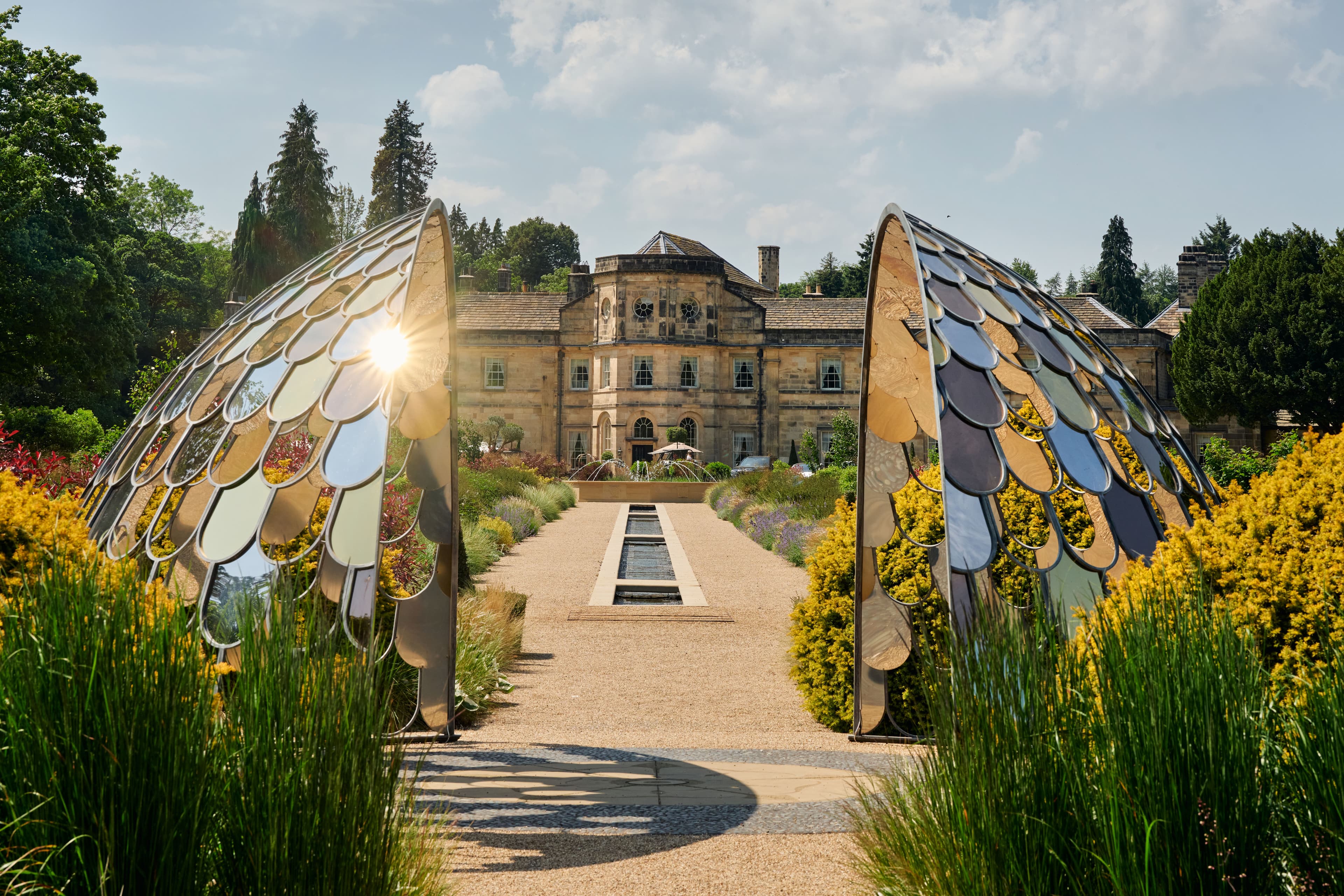 Reflective arches frame the entrance to Grantley Hall, surrounded by vibrant gardens and a tranquil water feature.