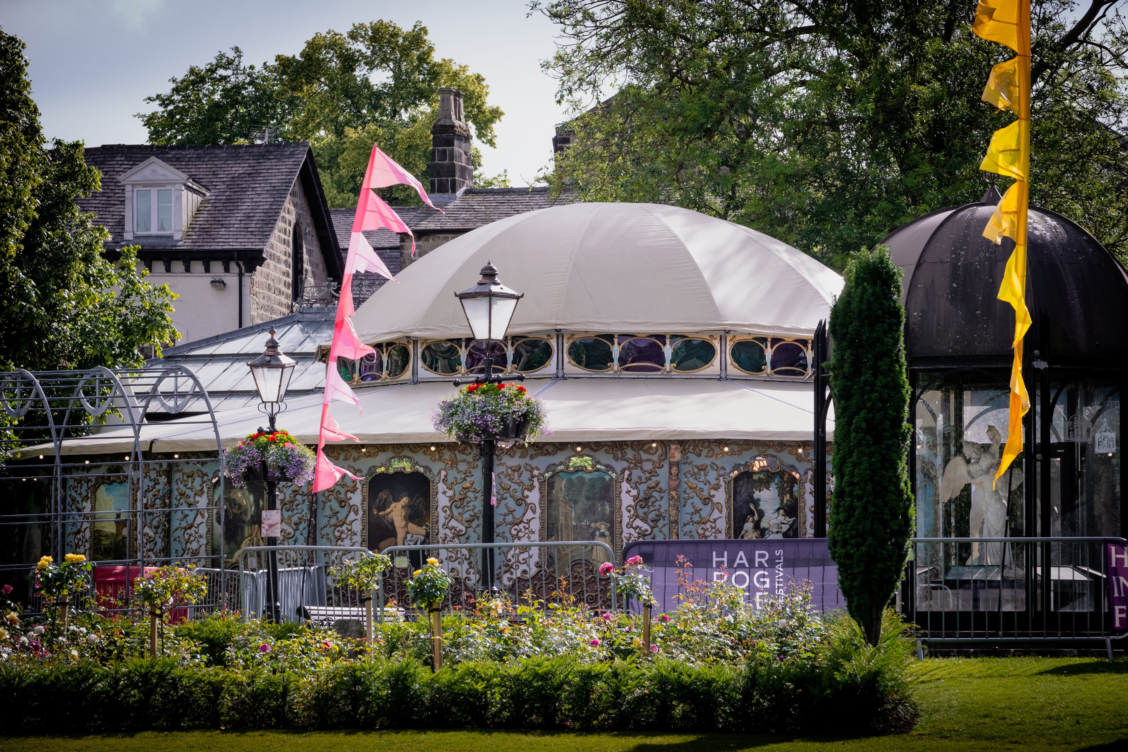 Spiegeltent in Harrogate, adorned with colorful flags and flowers, set against a backdrop of lush greenery and charming architecture.