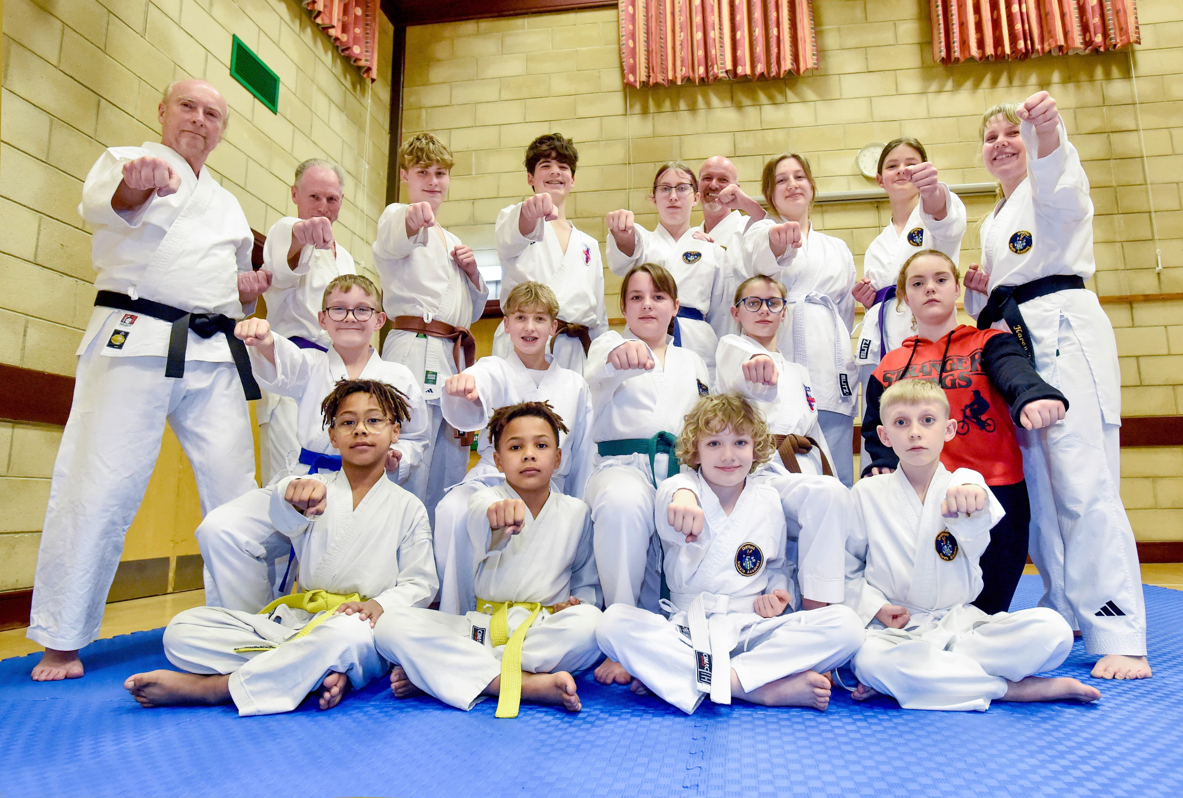 A diverse group of karate students and instructors in Driffield, wearing uniforms and striking poses on a blue mat.