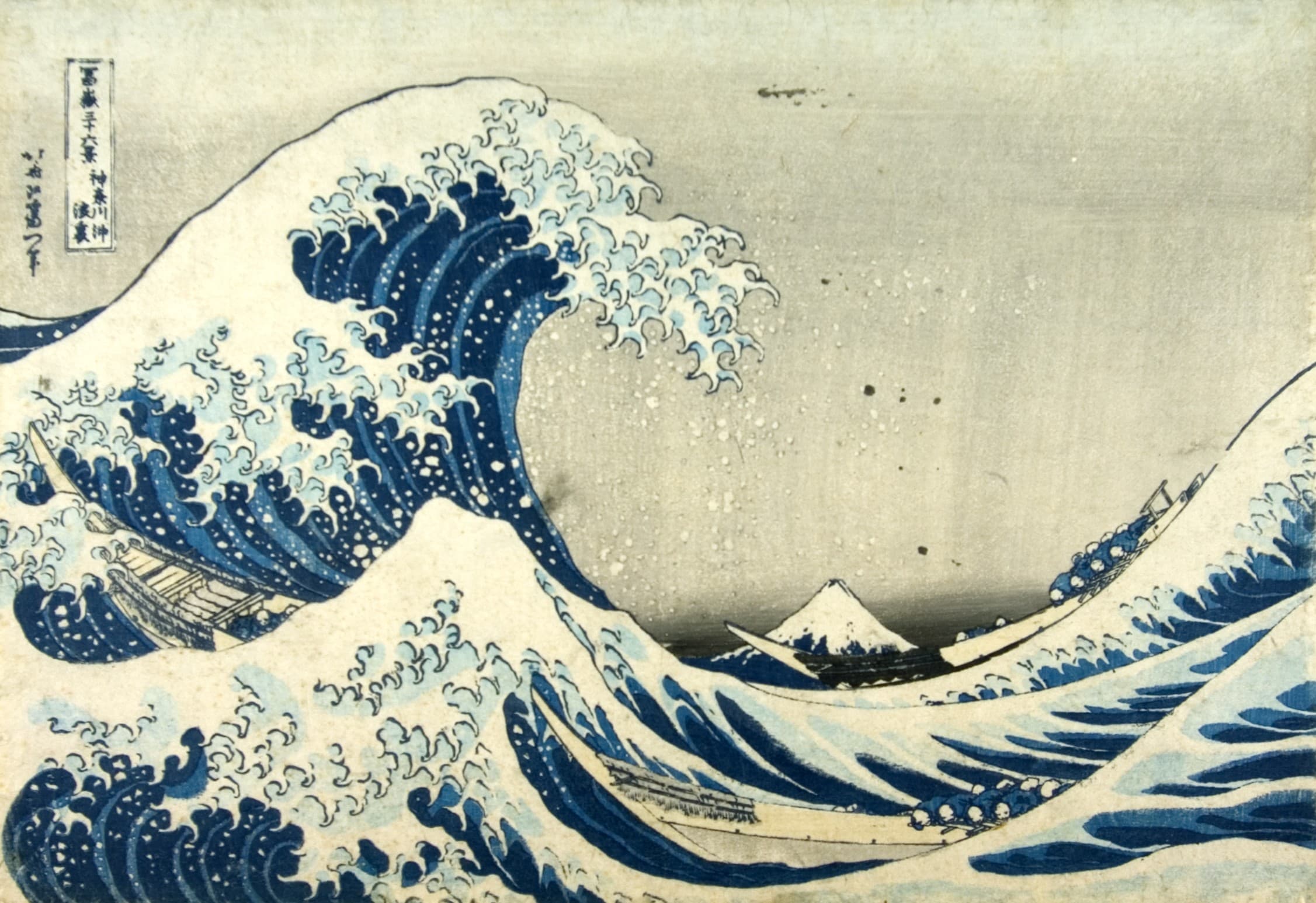 Dynamic blue waves crash against boats, with a distant mountain peak under a cloudy sky, showcasing traditional Japanese art.