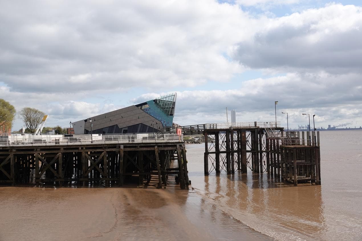 Victoria Pier with modern architecture in the background, reflecting on the water under a cloudy sky.