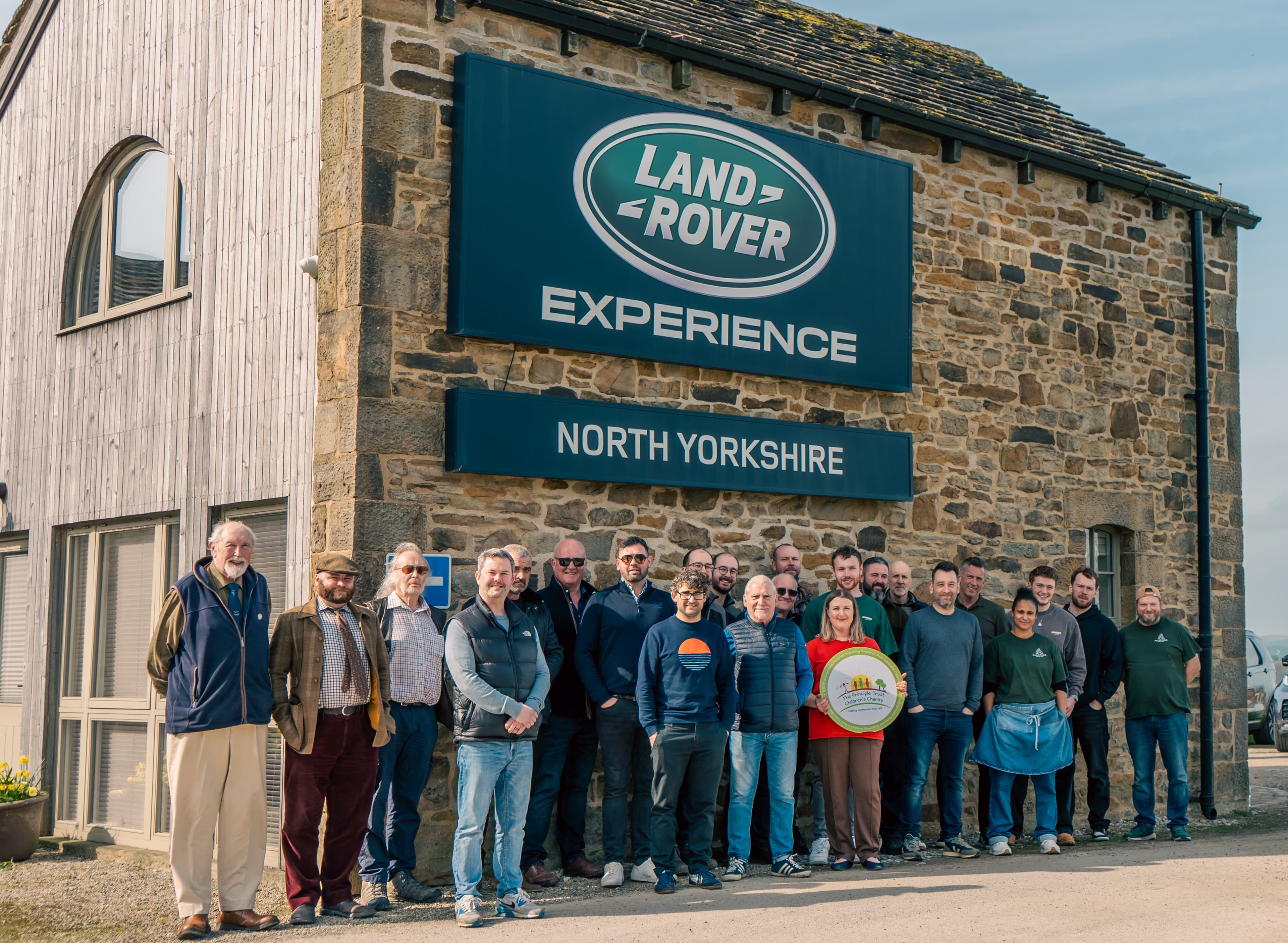 Group of participants posing outside the Land Rover Experience center in North Yorkshire, smiling and holding a charity plaque.
