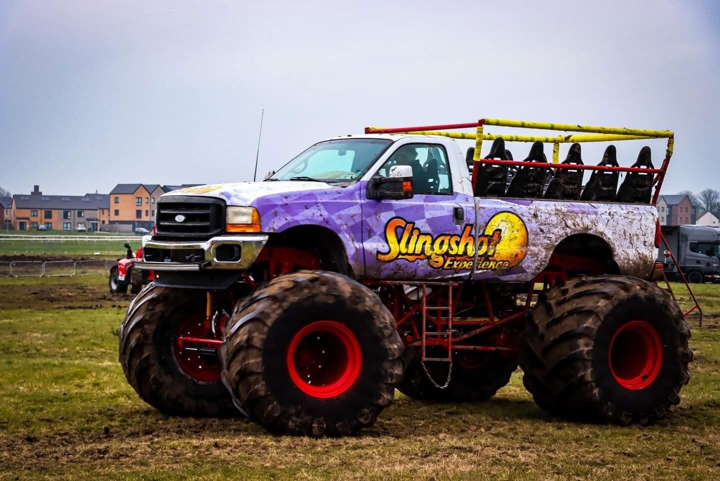 A vibrant purple monster truck with oversized tires sits on a grassy field, ready for action at a motorsport event.