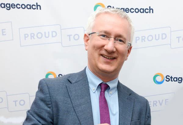 Smiling man in a suit stands in front of a Stagecoach backdrop, exuding a friendly and welcoming atmosphere.