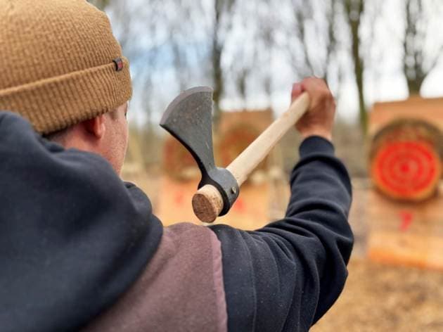 A person in a beanie prepares to throw an axe at wooden targets in a wooded area, showcasing adventure at a Yorkshire water park.