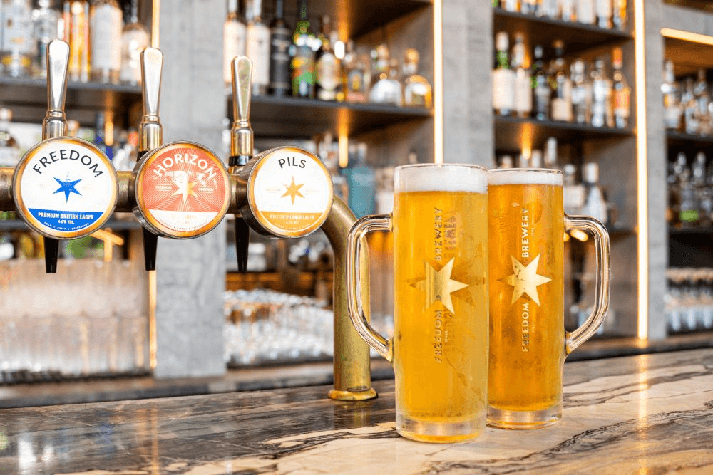 Two frosty pints of lager with star logos sit on a polished bar top, surrounded by shelves of spirits in a vibrant Sheffield pub.