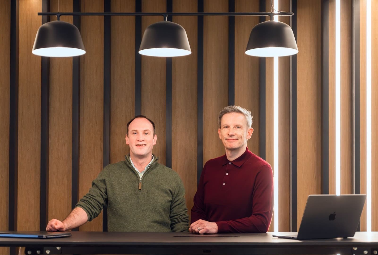 Two professionals stand confidently at a sleek, modern workspace with wooden paneling and stylish lighting in Leeds.