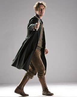 A man in a long coat and boots holds a futuristic device, set against a neutral backdrop, evoking a sci-fi theme.