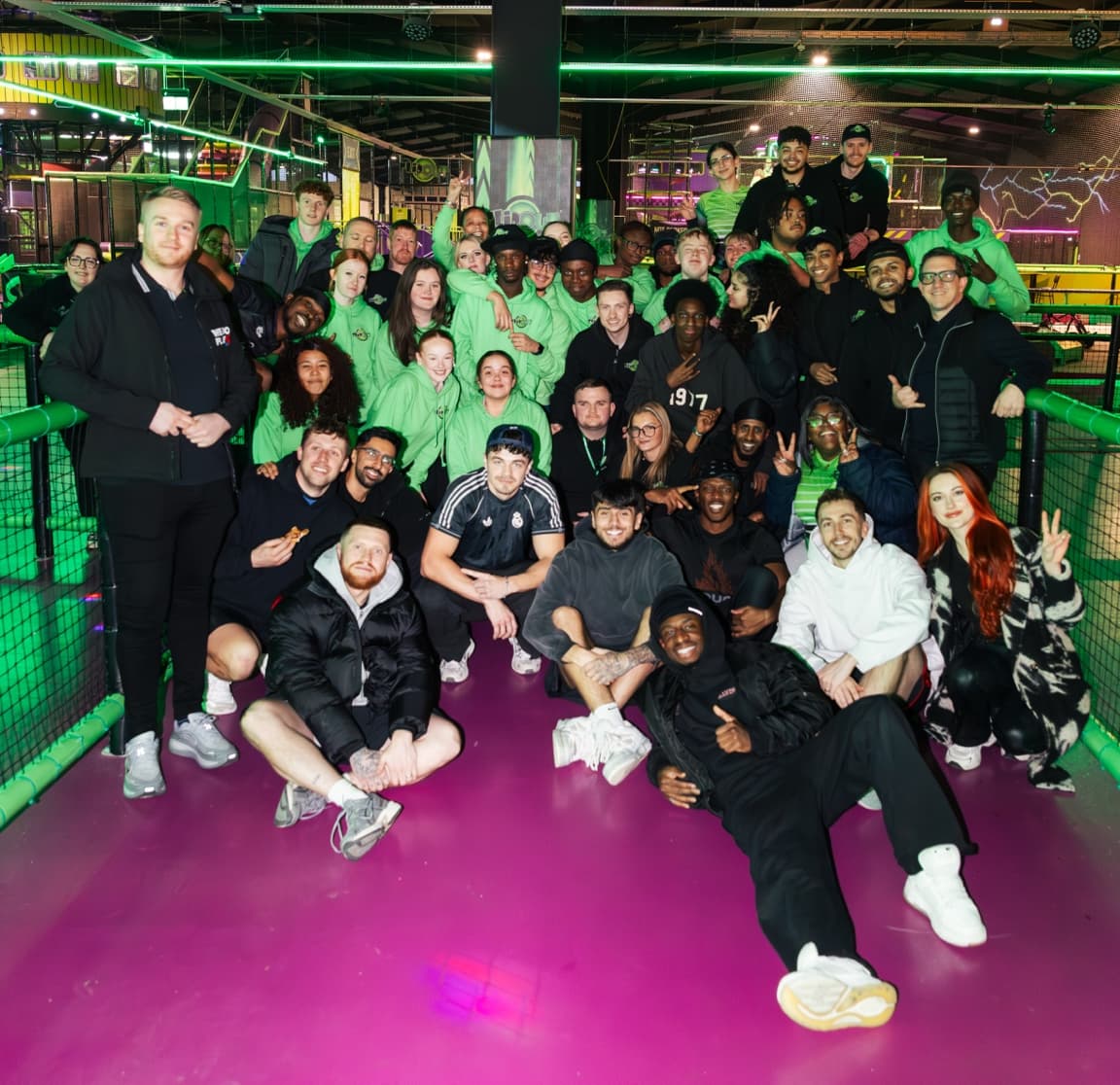 A large group of people, including the Sidemen, poses together in a vibrant indoor trampoline park at Flip Out Leeds.