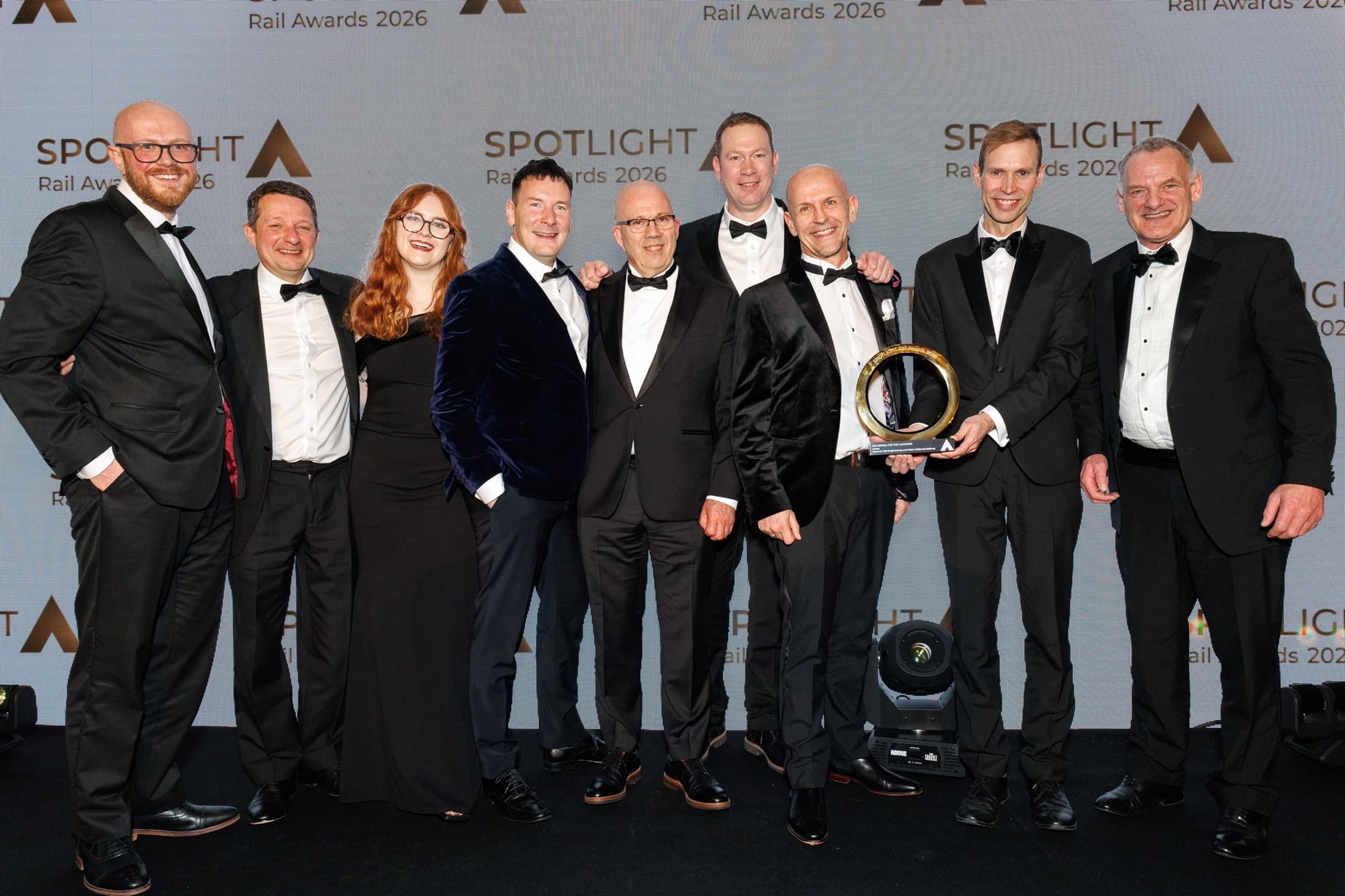 A group of elegantly dressed individuals poses together, holding an award at the Rail Awards 2026 event.