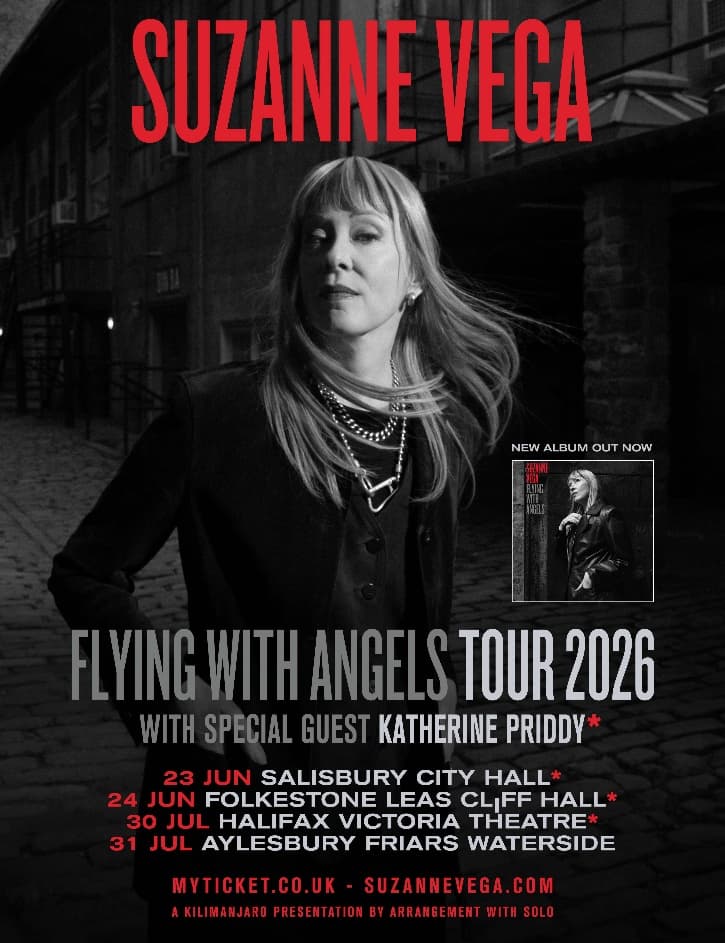 Suzanne Vega stands confidently against a brick wall, promoting her upcoming UK tour with a moody urban backdrop.