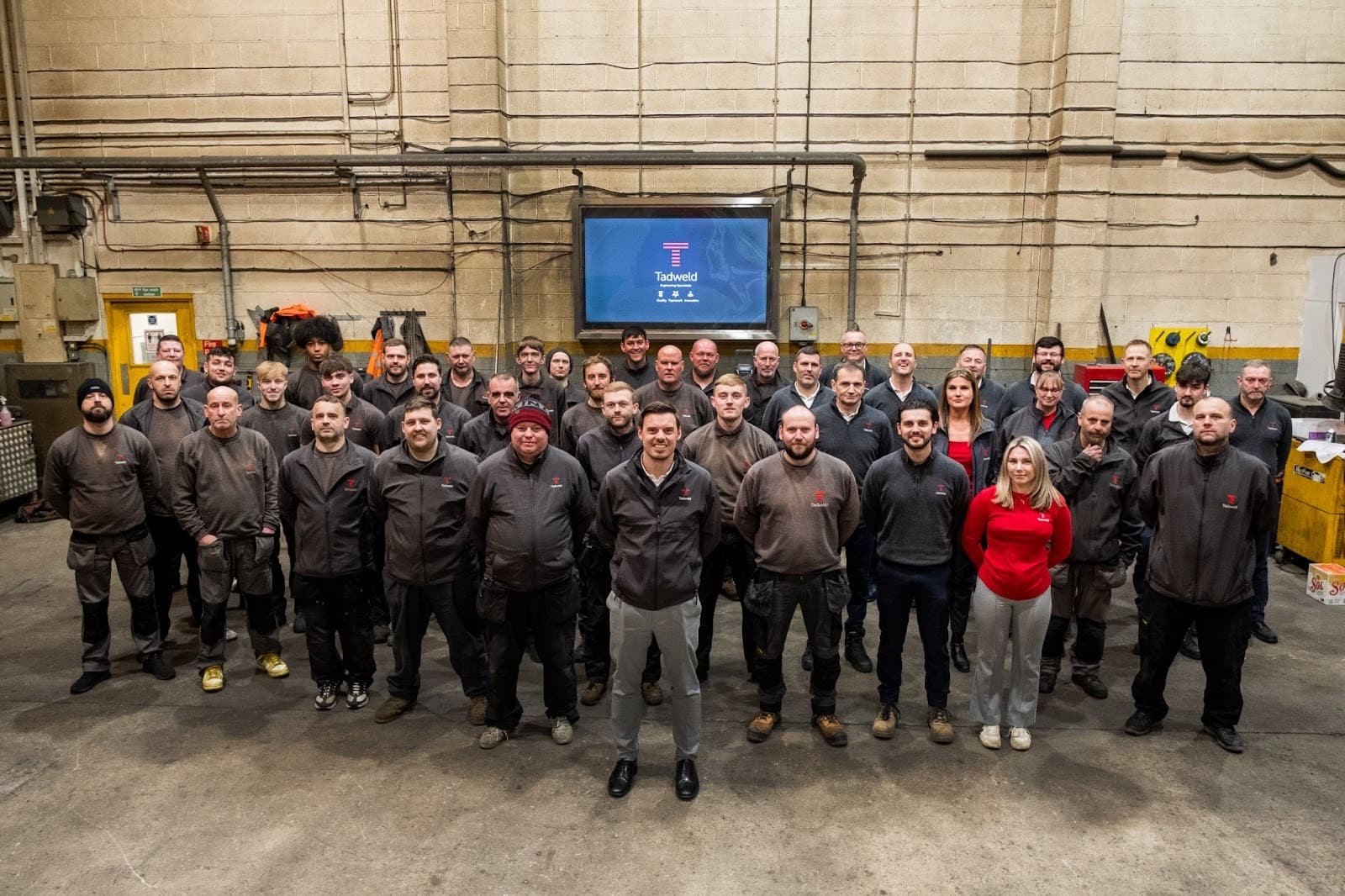 A diverse team stands together in a spacious workshop, showcasing teamwork and dedication at Tadweld in Yorkshire.