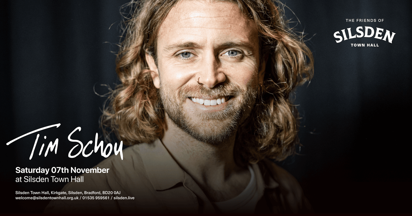 Tim Schou smiles warmly, promoting his intimate performance at Silsden Town Hall, set against a dark, inviting backdrop.