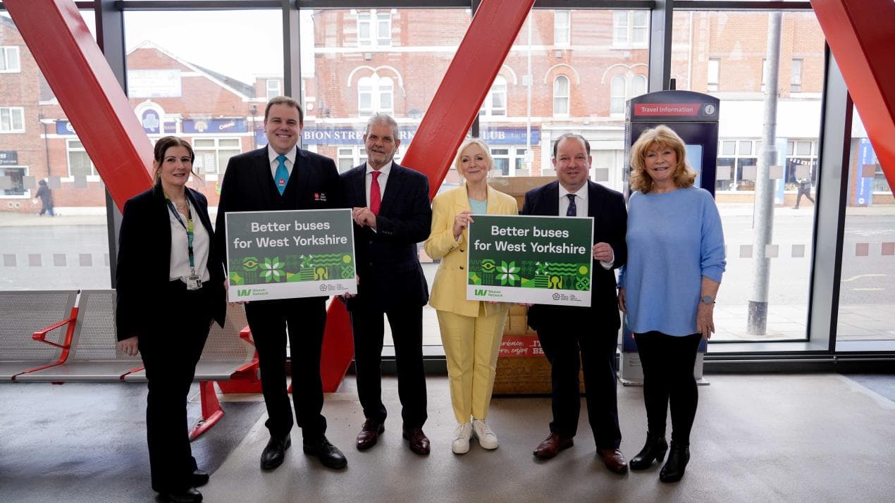 Group of five people holding signs promoting better bus services, set in a modern transport hub in Wakefield.