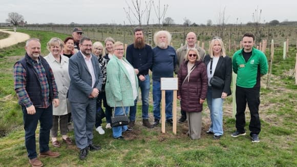 A group of people gathered around a tree planting site in York, with newly planted saplings and a sign in the background.