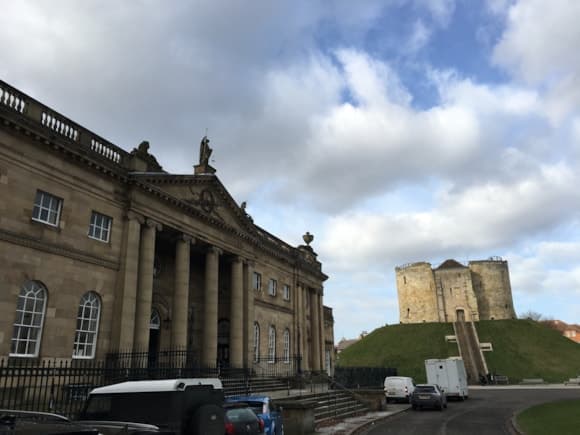 Historic courthouse with grand columns, overlooking the iconic York Castle under a cloudy sky.