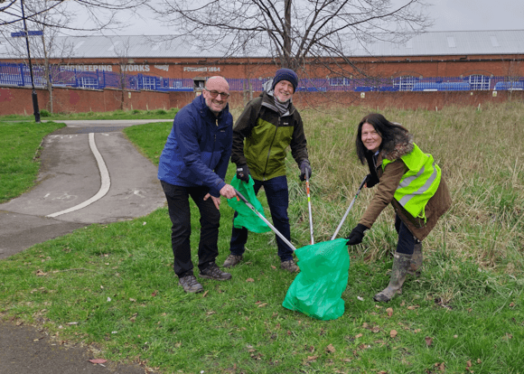 Three volunteers in bright jackets collect litter in a grassy area near a pathway in York, promoting community clean-up efforts.