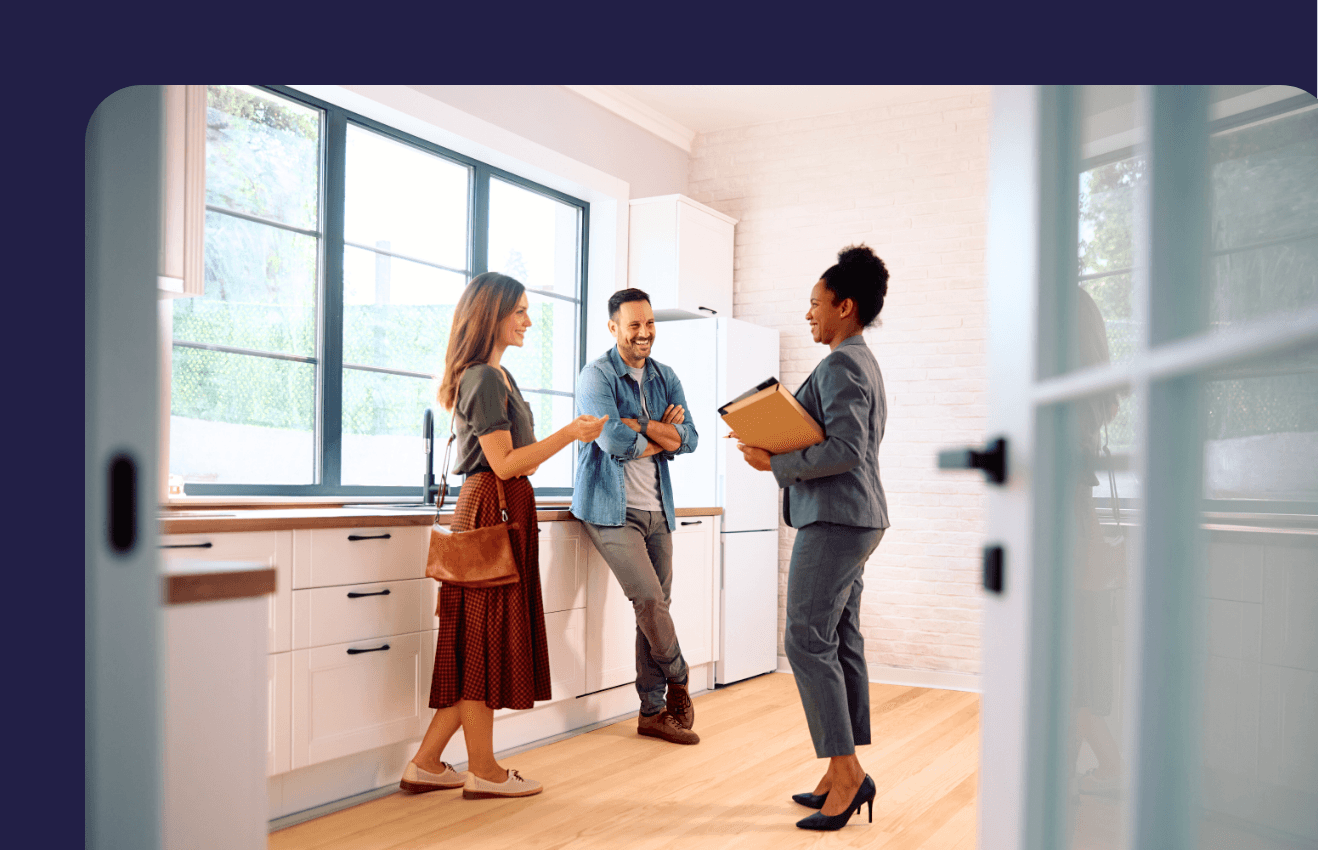 Three people engage in conversation in a bright, modern kitchen with large windows and warm wooden floors.