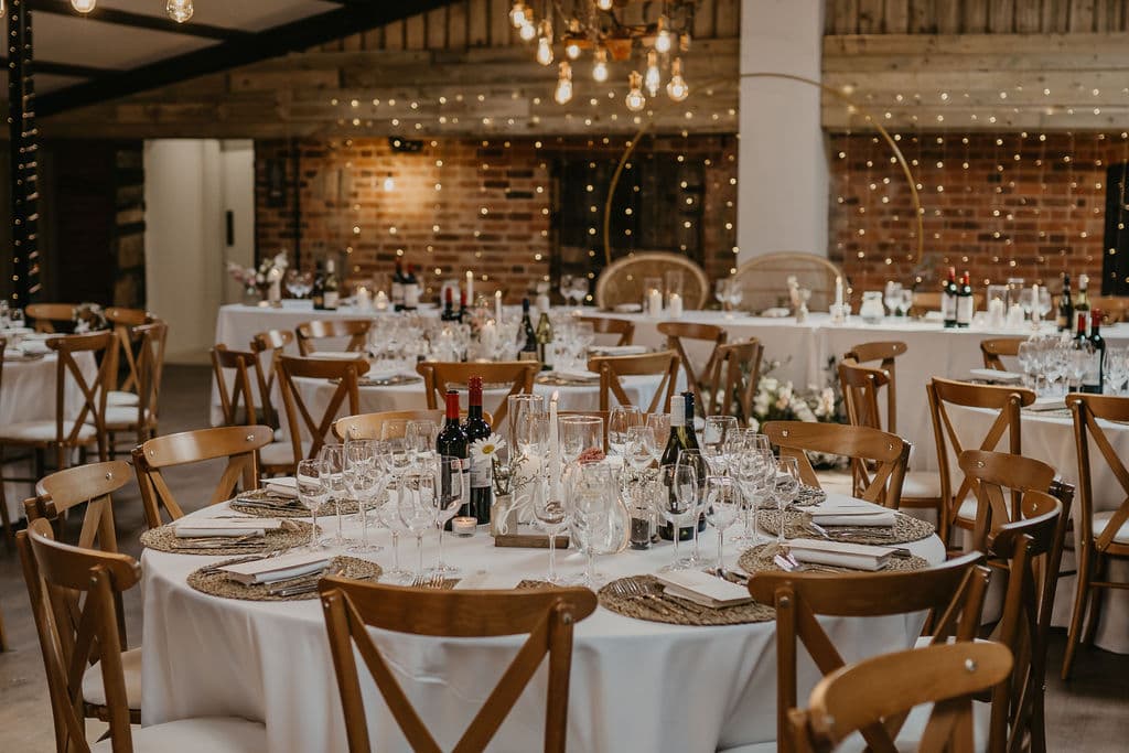 Elegant round tables set with fine glassware and rustic wooden chairs, adorned with soft lighting and floral centerpieces at Deighton Lodge.