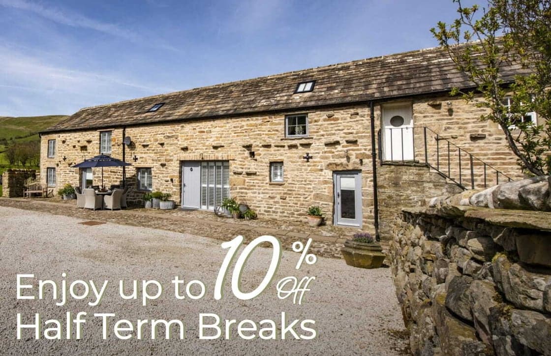 Charming stone cottage with a rustic facade, surrounded by greenery and gravel, set against a picturesque Yorkshire landscape.