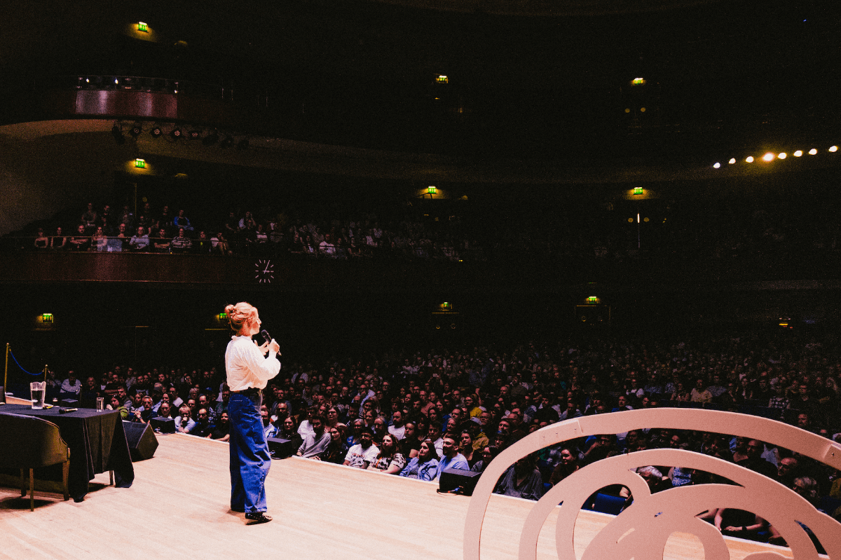 Speaker on stage addressing large audience in grand theatre
