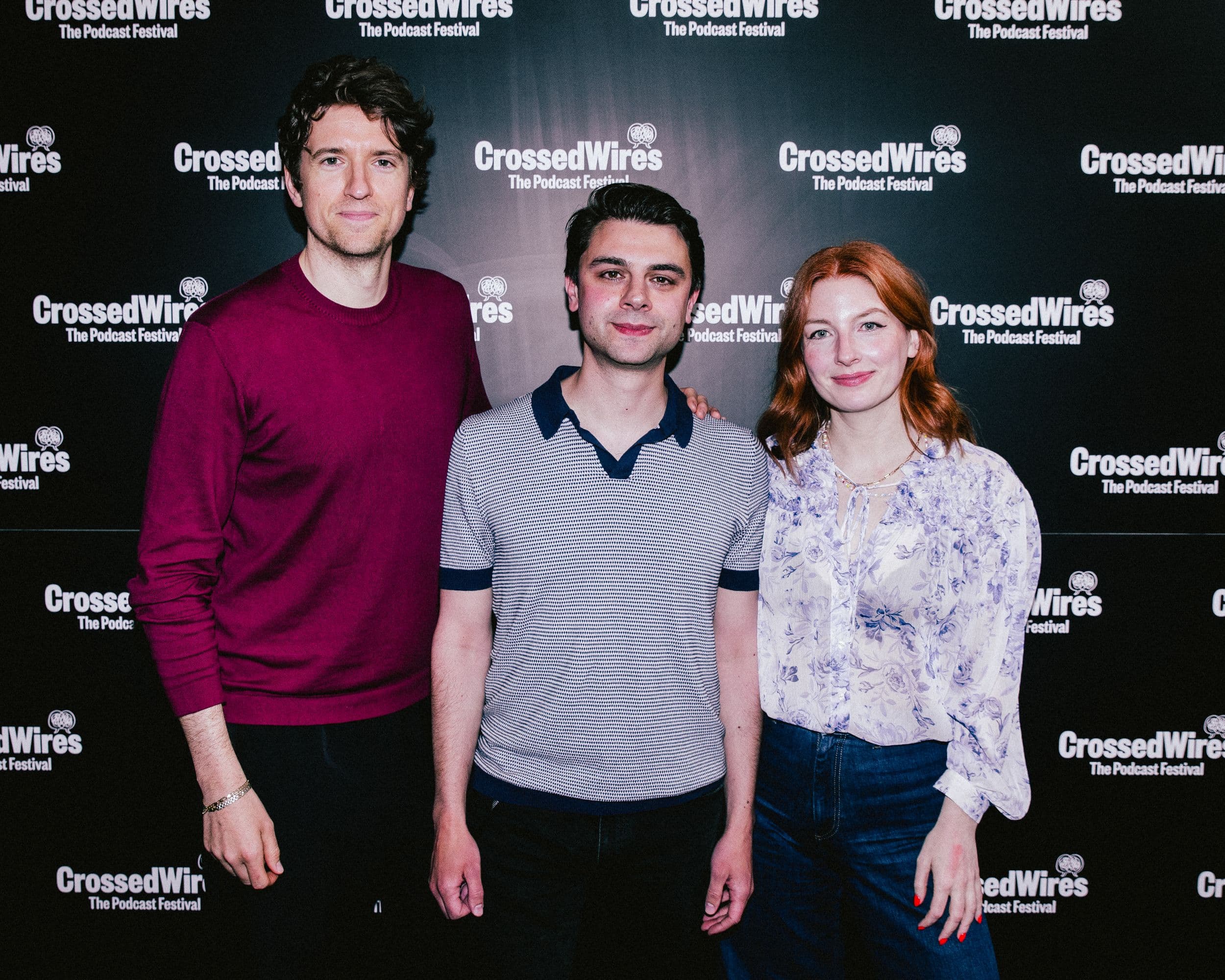Three people smiling in front of a Crossed Wires festival backdrop