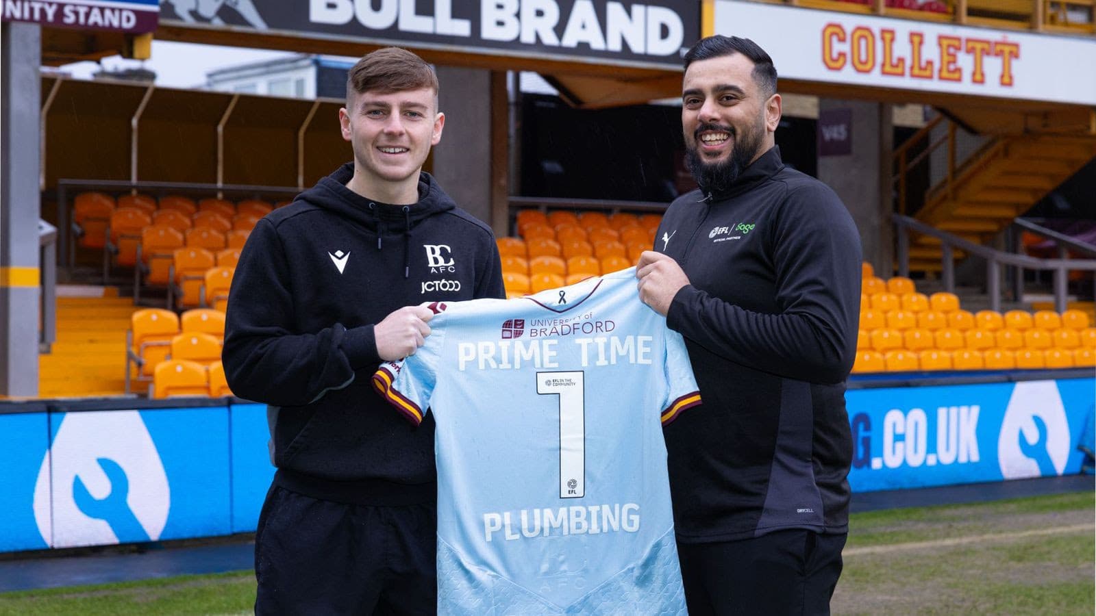 Two smiling men holding a football jersey at a stadium