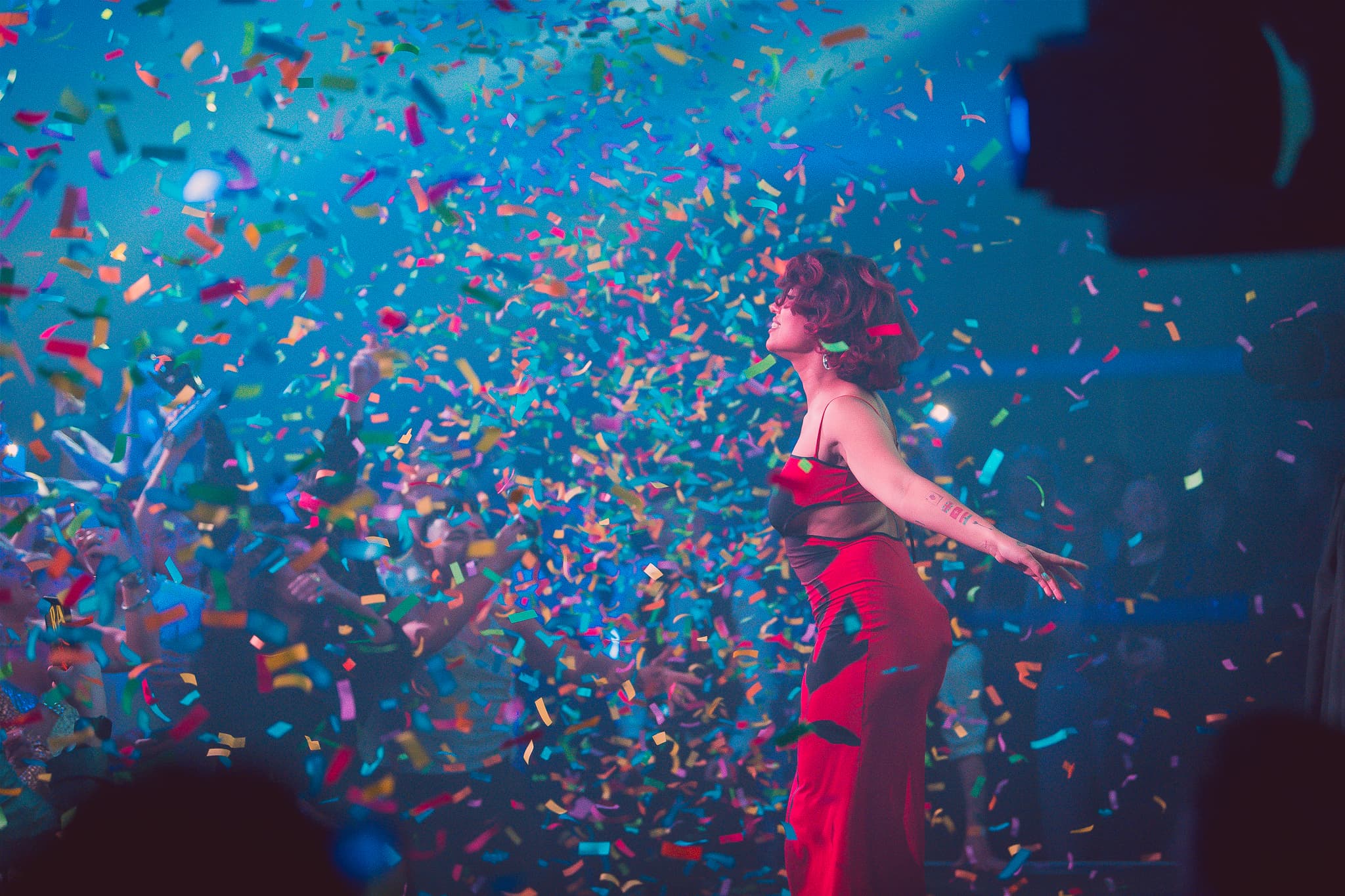 Woman in red dress dancing amid colorful confetti on stage