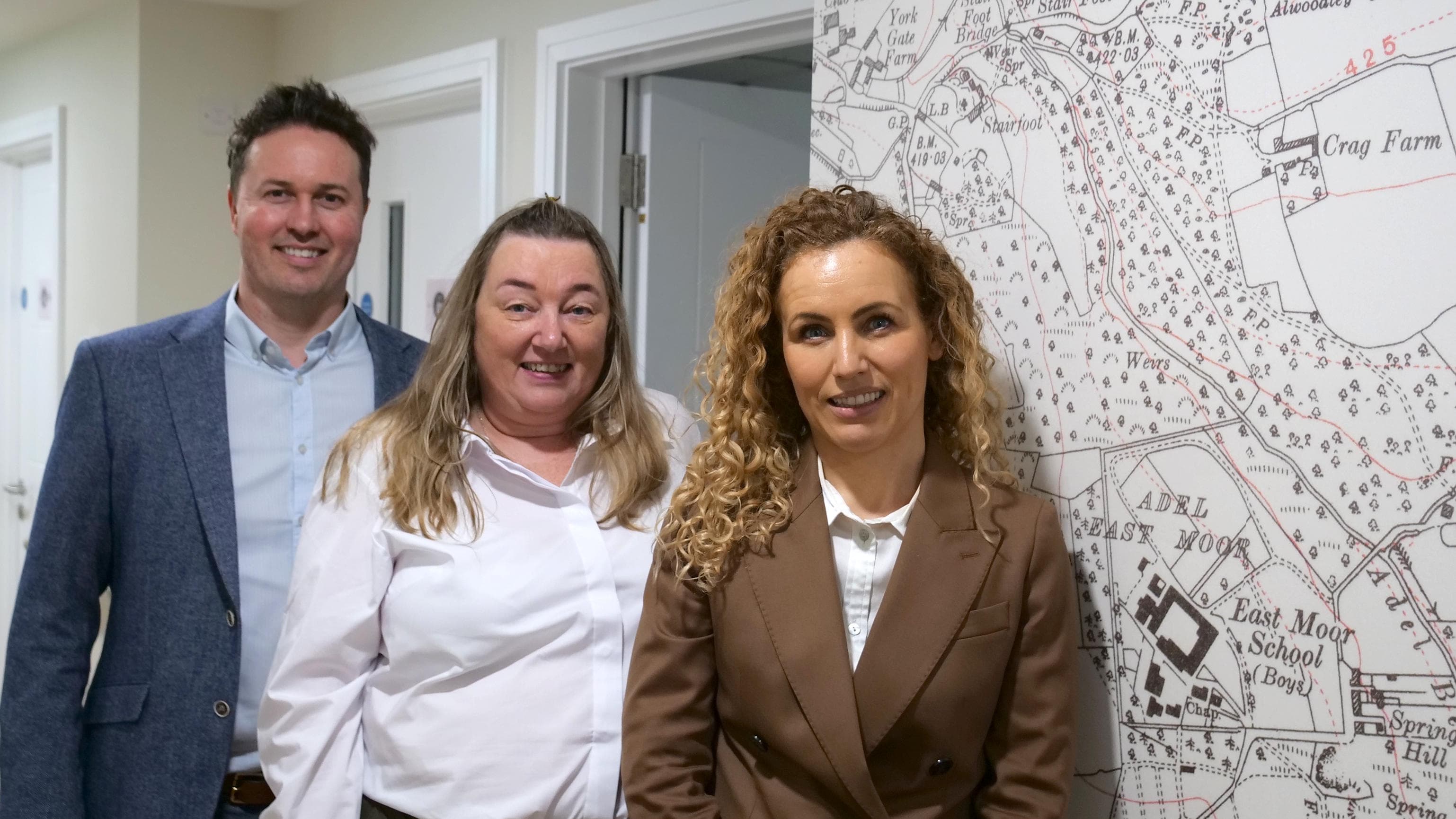 Three people smiling in front of a vintage Yorkshire map