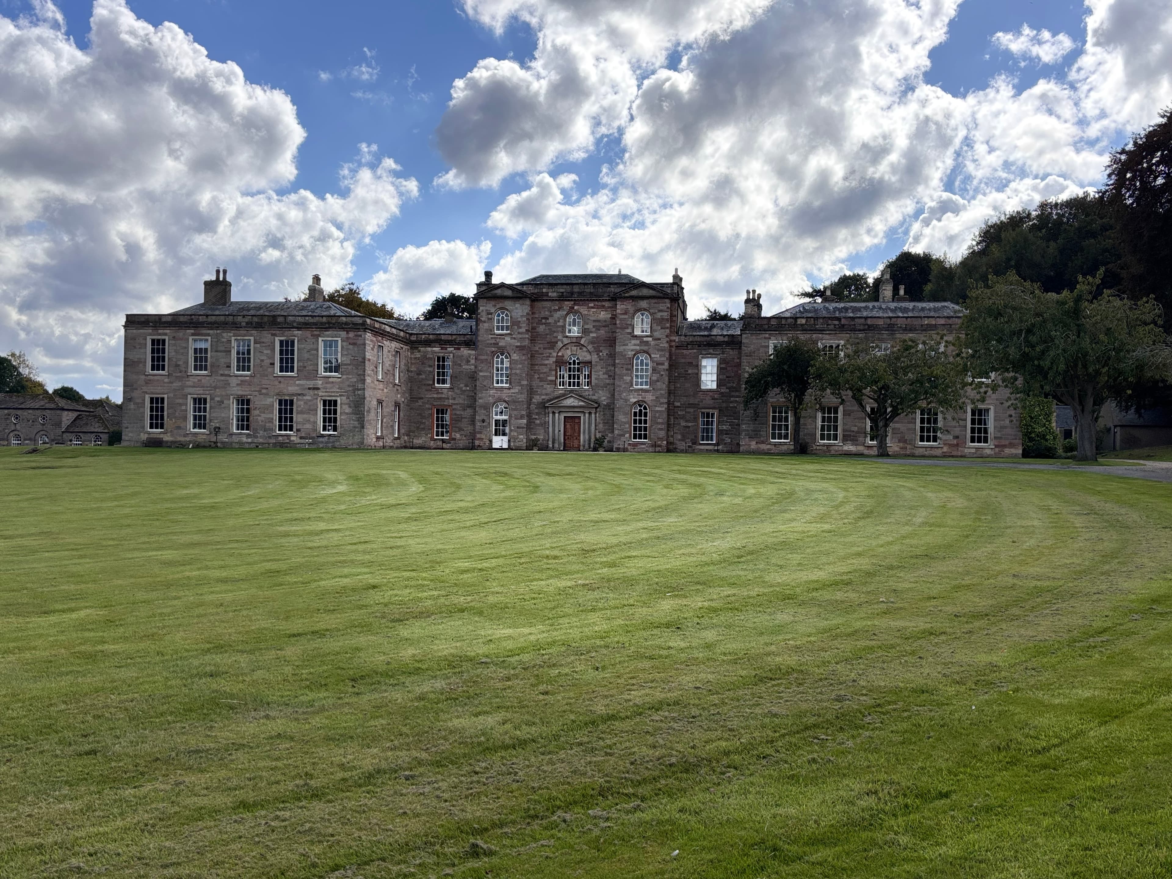 Historic stone manor with large lawn under cloudy sky