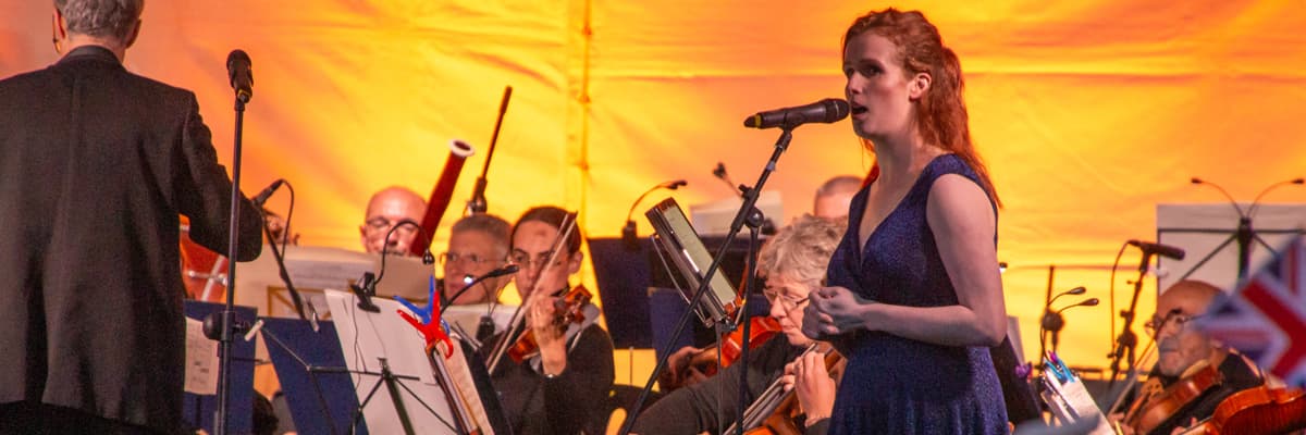 Singer in blue dress performing with orchestra under warm lighting