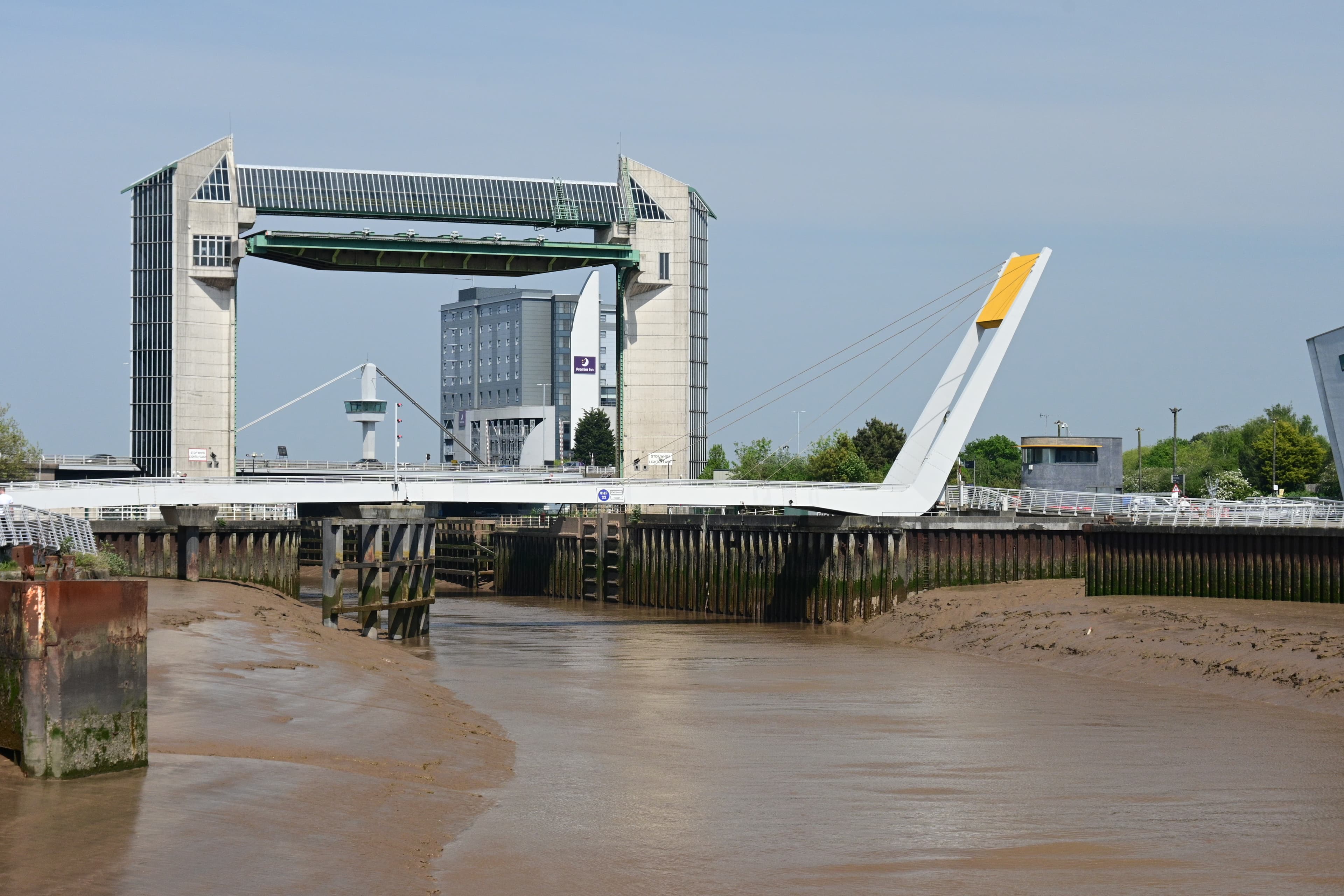 Modern swing bridge over muddy river with industrial backdrop
