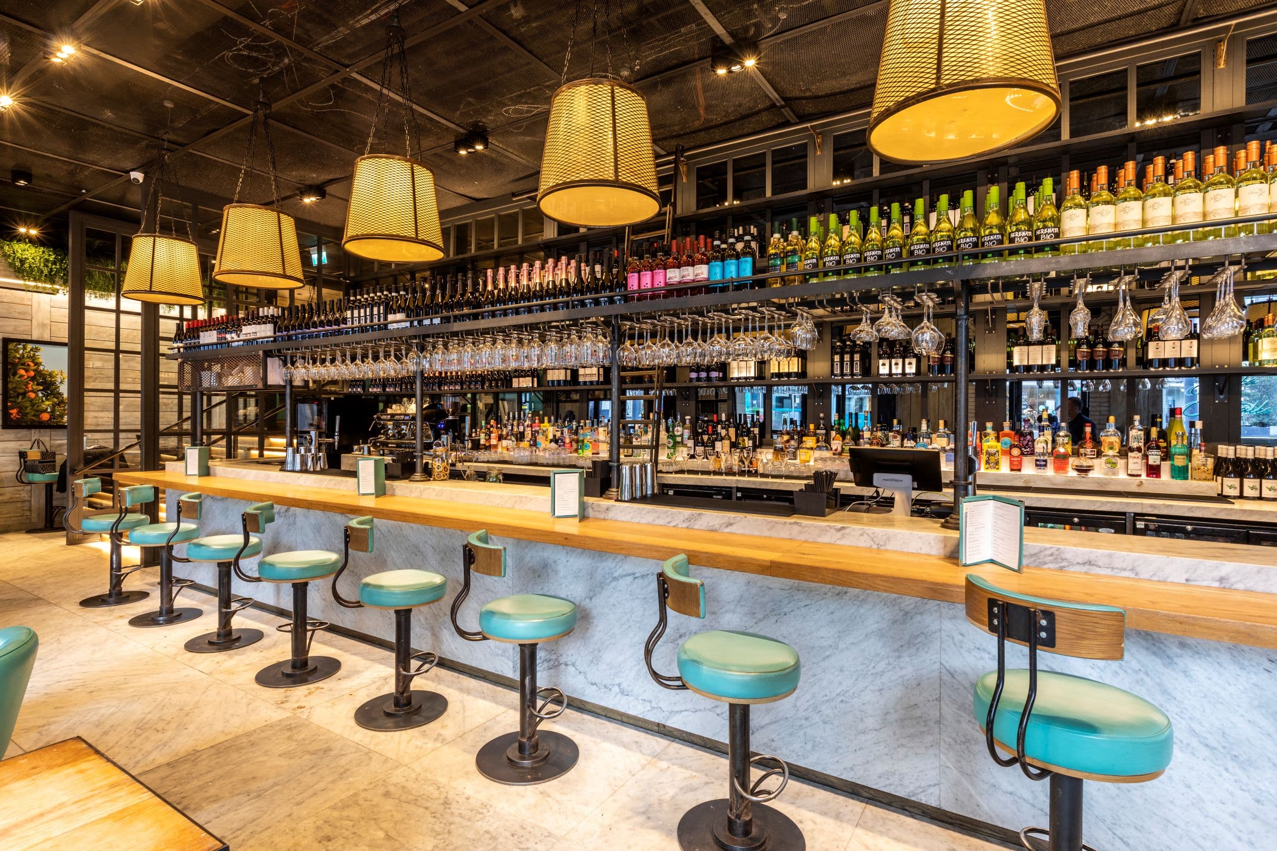 Modern bar with teal stools, hanging lights, and colorful bottles