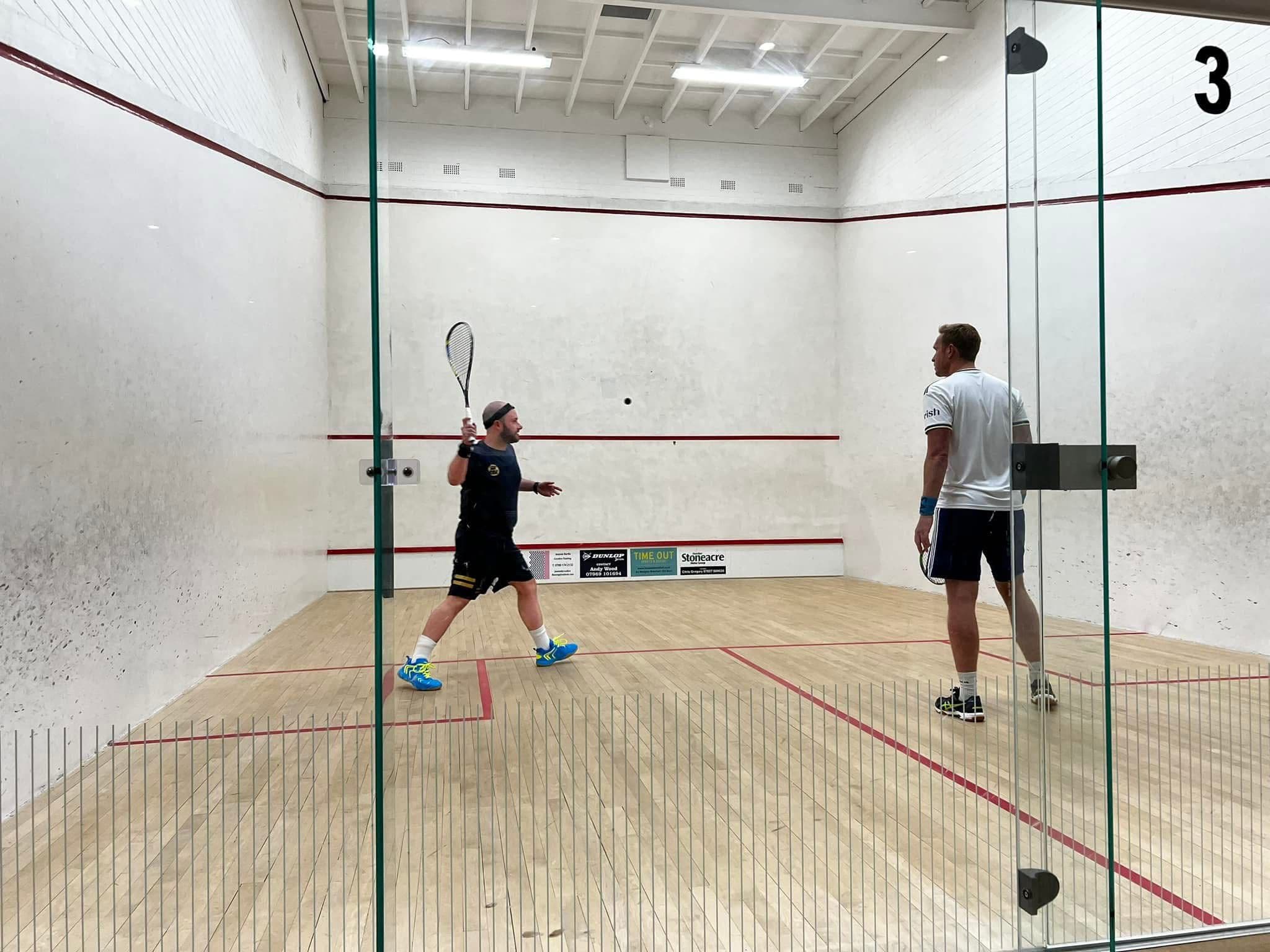 Two men playing squash in a white-walled indoor court