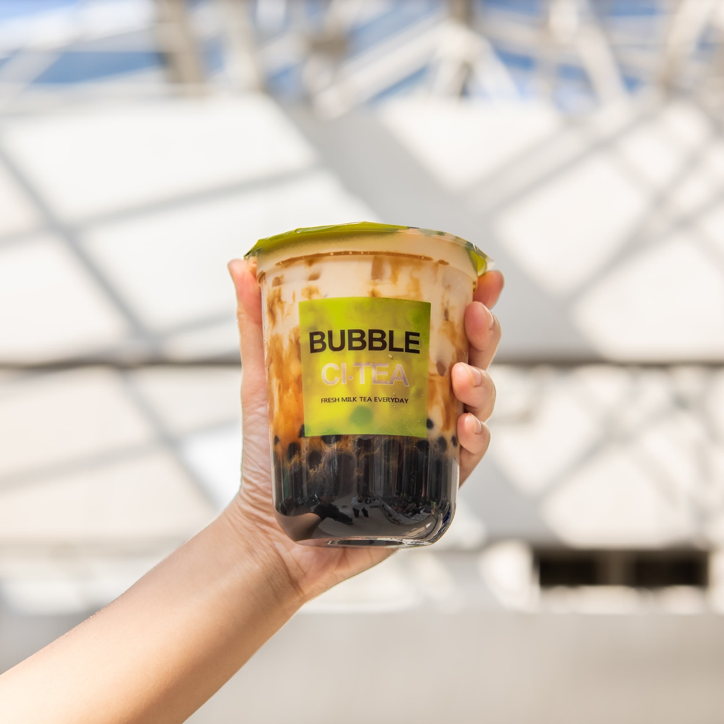 Hand holding bubble tea with tapioca pearls and green lid