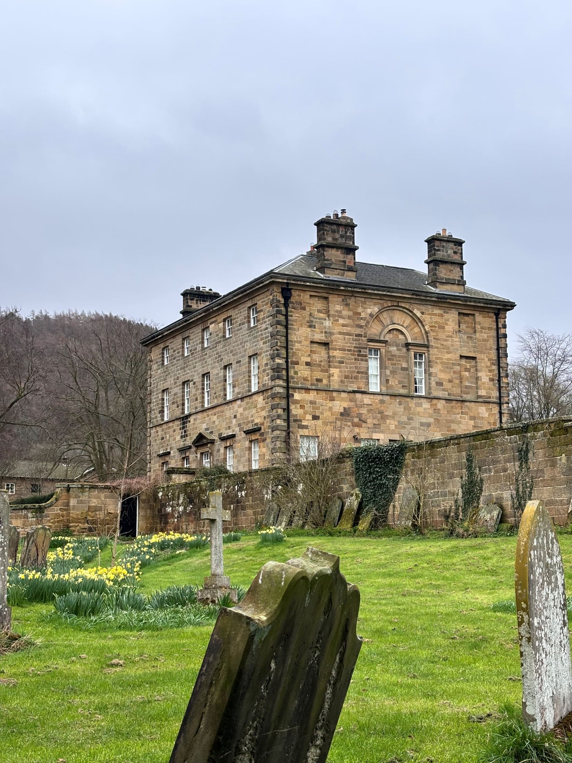 Historic stone manor house with arched window near old graves