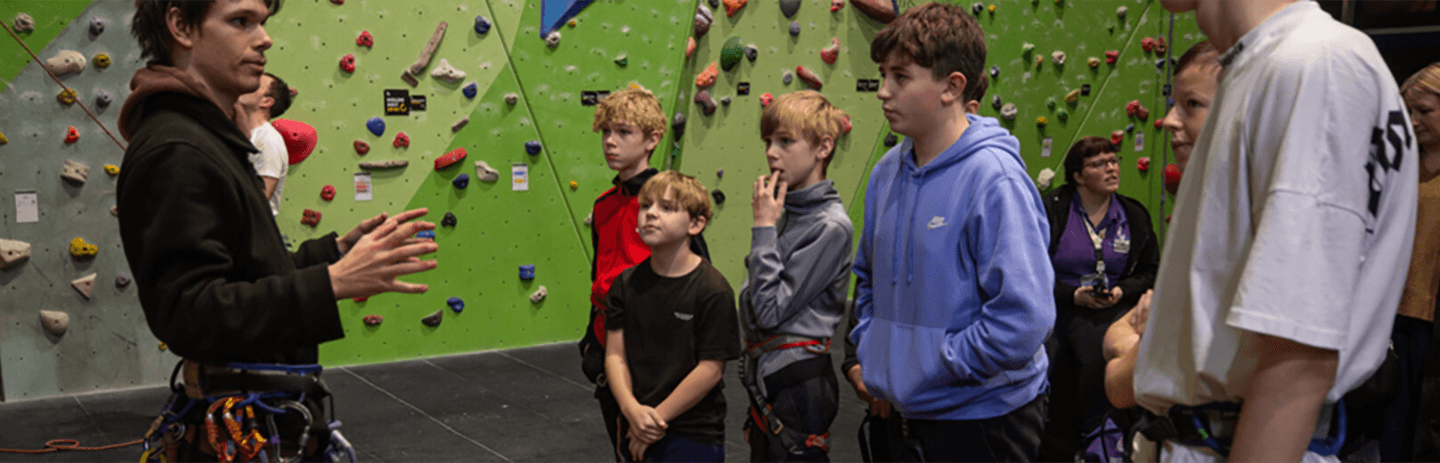Group of young people in climbing gear listening to an instructor