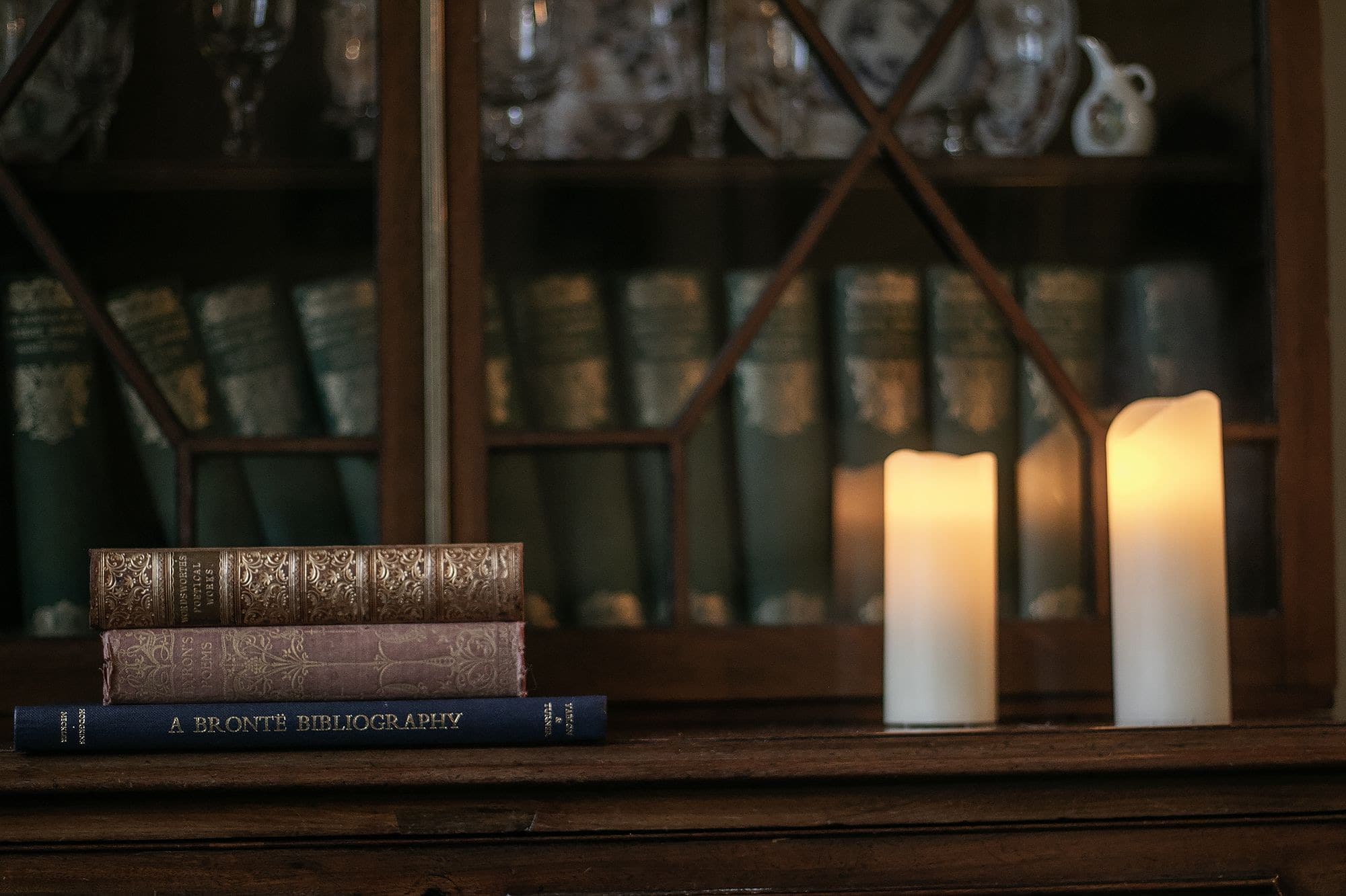 Candlelit bookshelf with classic hardcover books and glassware